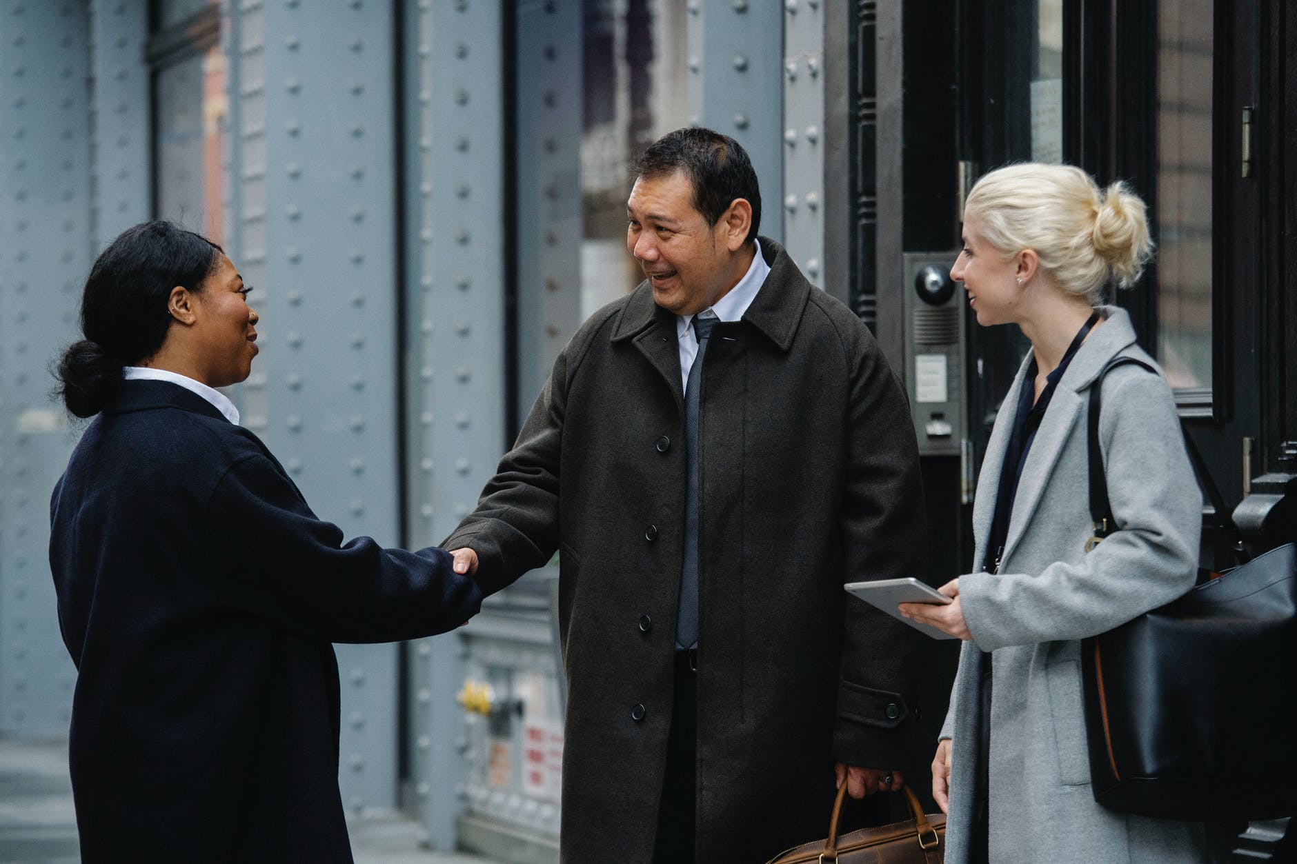 smiling diverse coworkers shaking hands on street before meeting